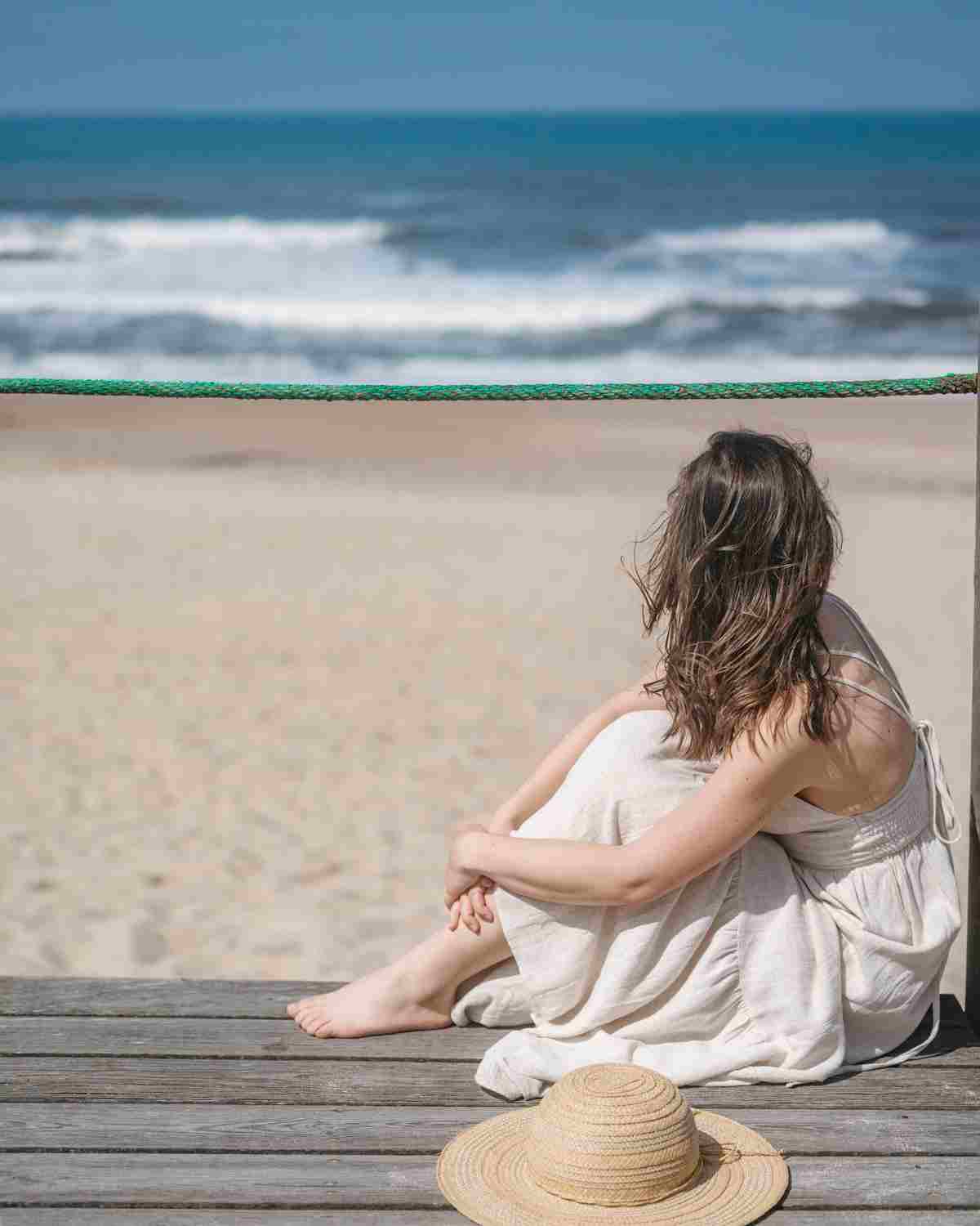 woman sitting on beach looking at the ocean in summer