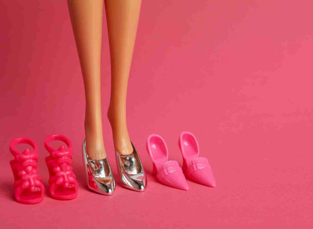 Barbie legs in silver shoes with pink sandals and pink pumps - cover image of Barbie Movie post